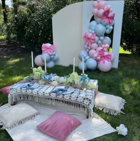 Outdoor celebration with a styled low table, cushions, flowers, and a pastel balloon backdrop